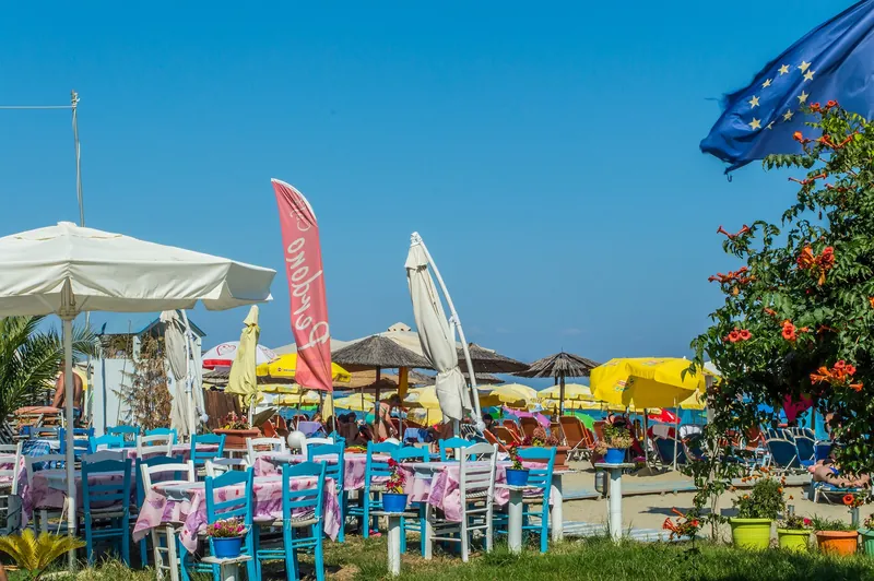 A taverna and umbrellas on the sand at Olympiaki Akti